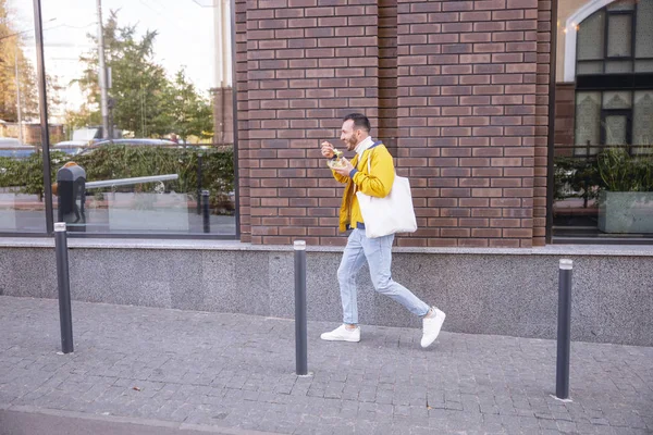 Joven hombre alegre caminando cerca del centro de negocios —  Fotos de Stock