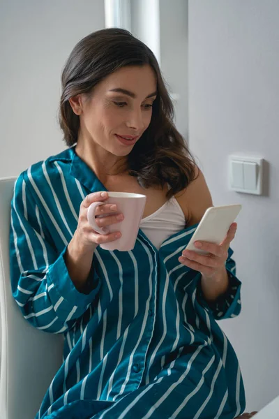 Mujer sonriente con teléfono inteligente y taza stock foto — Foto de Stock