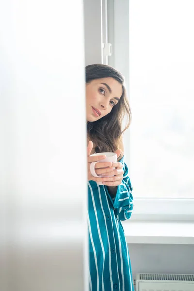 Jongedame met mok bij het raam stockfoto — Stockfoto