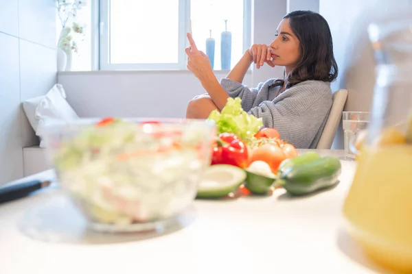 Femme au foyer réfléchie avec smartphone dans la cuisine stock photo — Photo