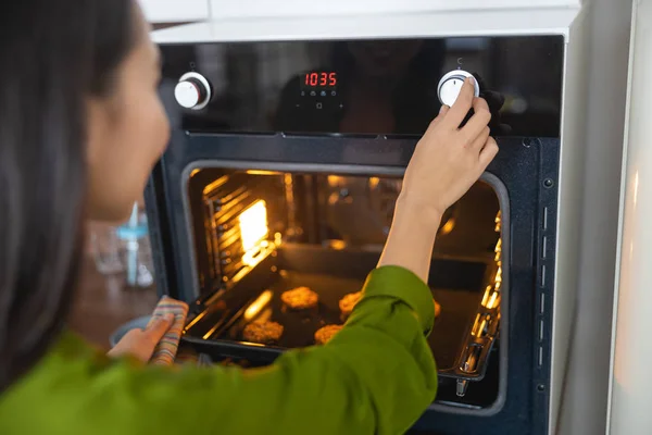 Young female cook adjusting the baking time — Stockfoto