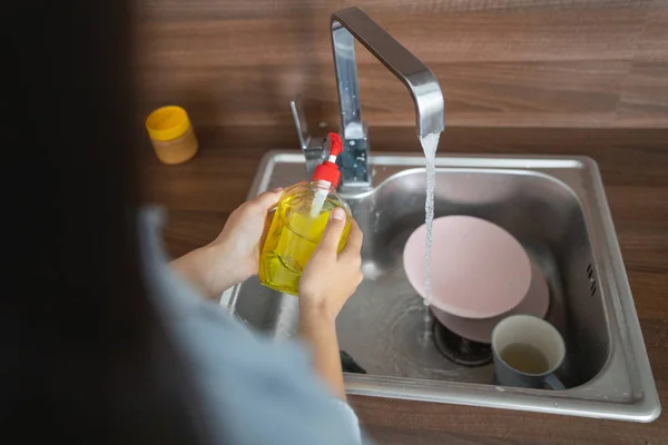 Mladá žena dívá na mytí nádobí tekutiny — Stock fotografie