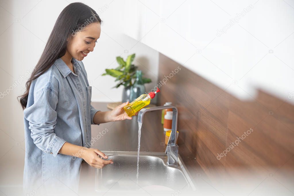 Happy young housewife standing in front of the sink
