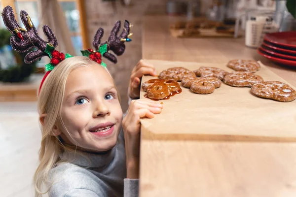 Ευτυχισμένο κορίτσι προσχολικής ηλικίας που στέκεται κοντά σε χριστουγεννιάτικα μπισκότα — Φωτογραφία Αρχείου