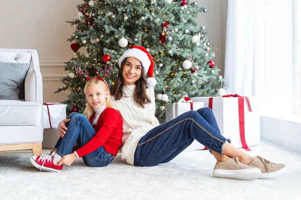 Mor och barn sitter nära julgranen — Stockfoto