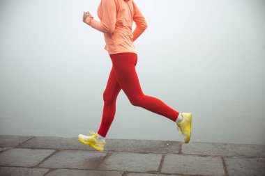 Kadın koşucu nehir boyunca kaldırımda koşuyor.