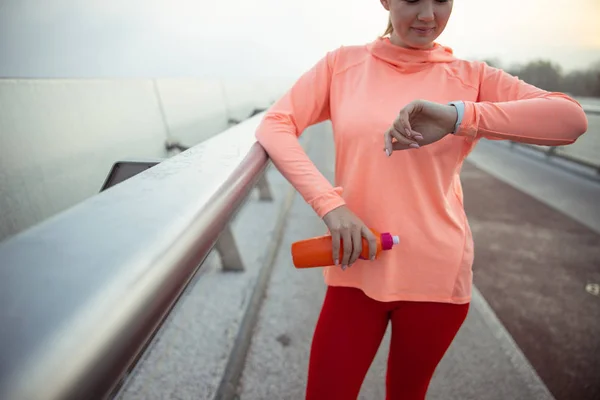 Dame sportive tenant une bouteille d'eau et regardant sa montre — Photo