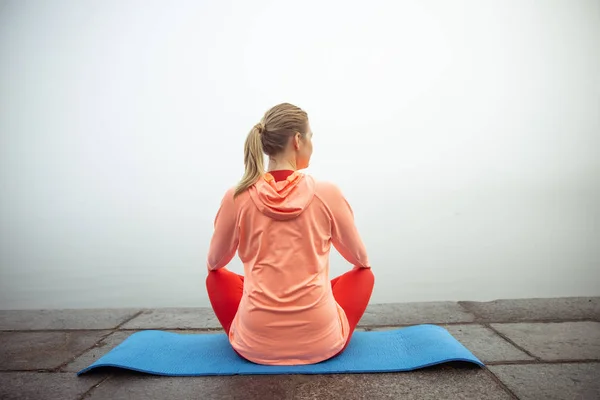 Mujer joven sentada en una esterilla de yoga al aire libre —  Fotos de Stock