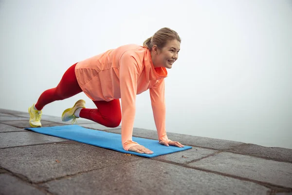 Souriant jeune femme faisant planche avec genou plié à l'extérieur — Photo