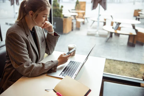 Mujer joven sonriente usando el teléfono celular en la cafetería — Foto de Stock