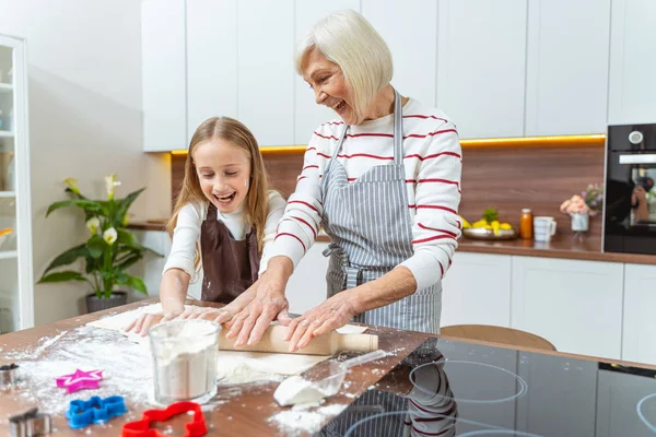 Glad hemmafru och hennes barnbarn plattar till degen — Stockfoto