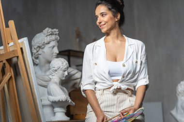 Gülümseyen kadın sanatçı sanat stüdyosunda resme bakıyor.