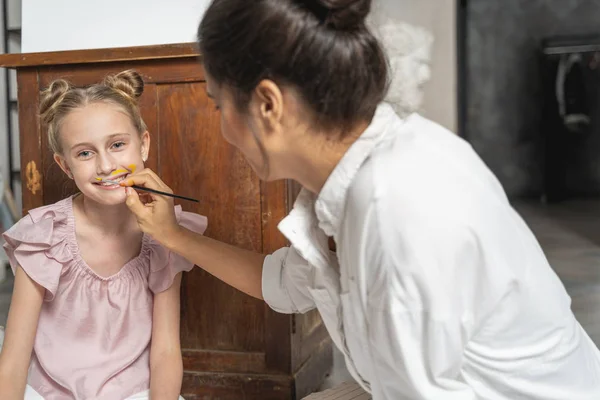 Caucasian woman painting face of little girl indoors — Stock Photo, Image