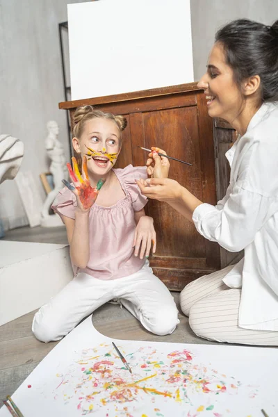 Femme caucasienne peinture visage de petite fille à l'intérieur — Photo