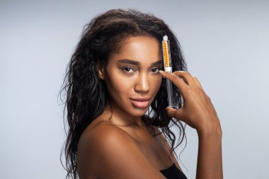 Şırıngayı elinde tutan kıvırcık saçlı büyüleyici Afro-Amerikan kadın.