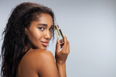 Kıvırcık saçlı güzel bir kadın şişeyi kozmetik sıvıyla saklıyor.