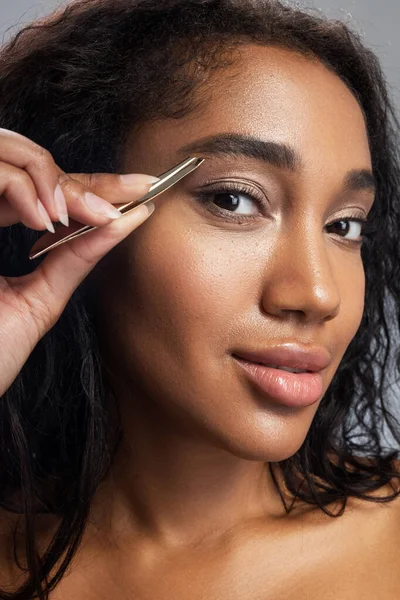 Cute Afro American woman plucking eyebrows with tweezers — Stock Photo, Image
