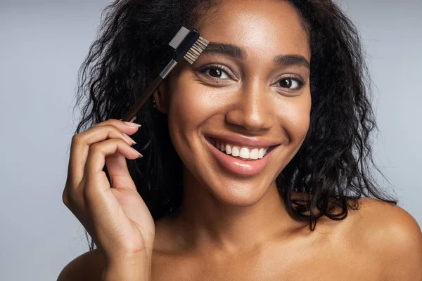 Sonriendo atractiva mujer afroamericana cepillándose las cejas — Foto de Stock