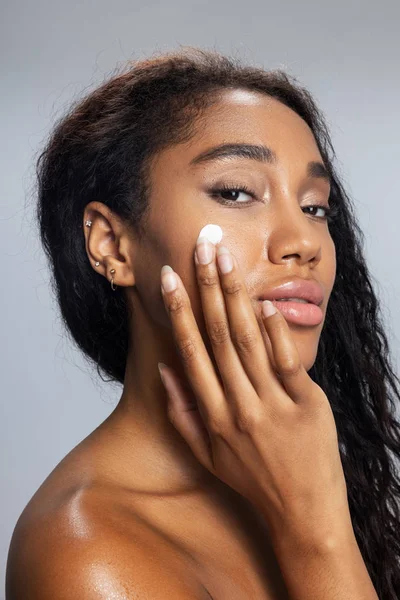 Maravillosa mujer afroamericana está aplicando crema facial — Foto de Stock