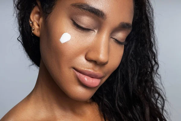 Relajada mujer afroamericana está aplicando crema facial — Foto de Stock