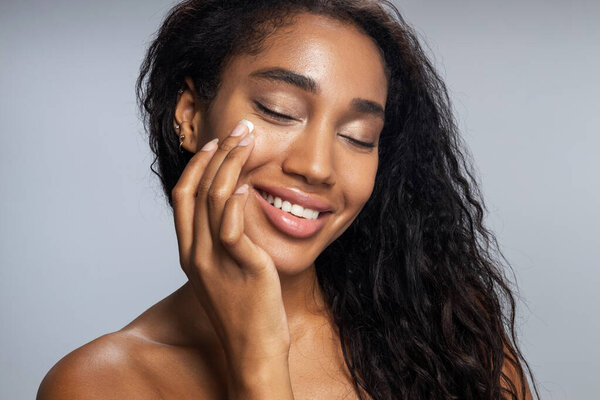 Красивая афро-женщина наносит крем для лица
