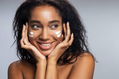 Yüz kremi süren seksi Afro-Amerikan kadın.