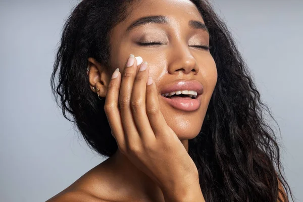 Mulher afro-americana sexy está aplicando creme facial — Fotografia de Stock