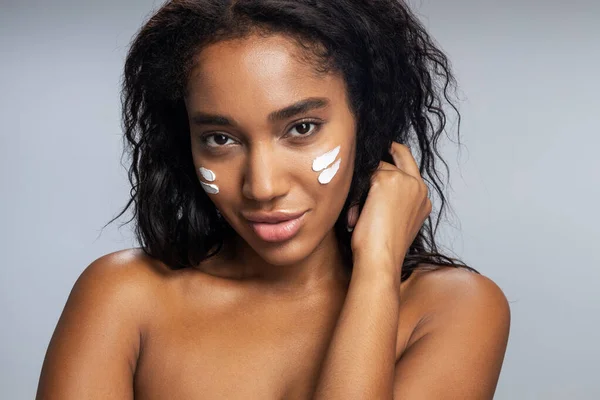 Calma atractiva mujer afroamericana aplicando crema facial — Foto de Stock