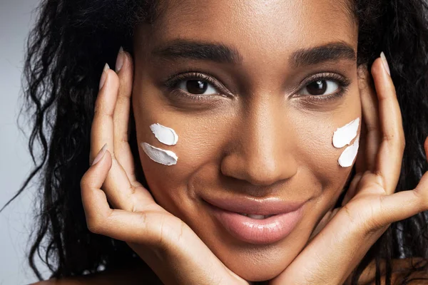 Sexy sorridente donna afro americana applicando crema viso — Foto Stock