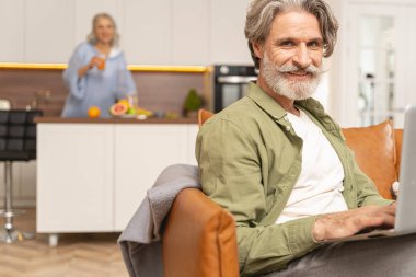 Kanepede dizüstü bilgisayarı olan bir adam oturuyor.