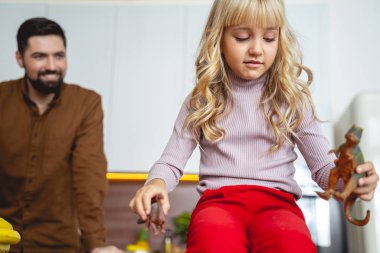 Neşeli adam kızının oyuncaklarla nasıl oynadığını izliyor.
