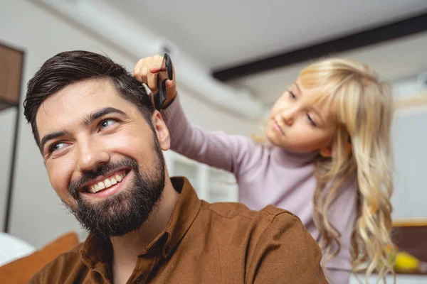 Petite fille mignonne brossant les cheveux de son père — Photo