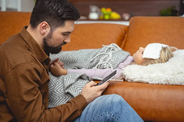 Father sitting beside his sick daughter and using cellphone — Stock Photo, Image