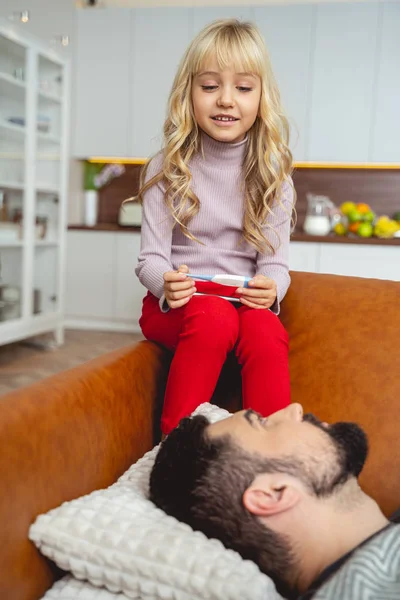 Маленька дівчинка з термометром сидить біля хворого батька — стокове фото