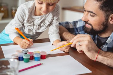 Gülümseyen baba kızının çizimini izliyor.