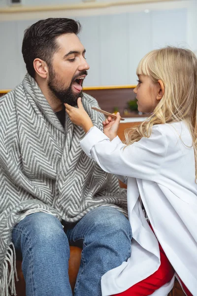 Niña usando la lengua de madera depresor para examinar enfermo padre — Foto de Stock