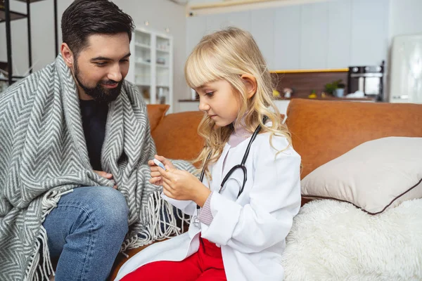 Niña tomando la temperatura del padre con termómetro — Foto de Stock