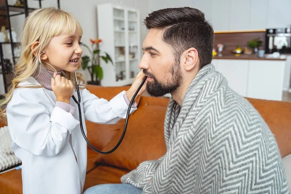 Menina bonito com estetoscópio jogando médico com o pai — Fotografia de Stock