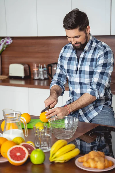 Leende ung man skära orange i köket — Stockfoto