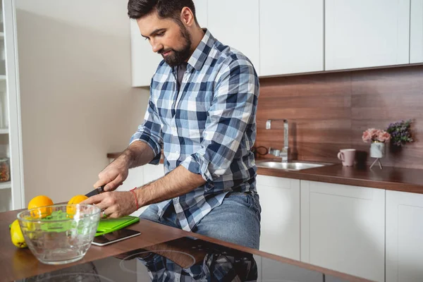 Skäggig ung man skära orange i köket — Stockfoto