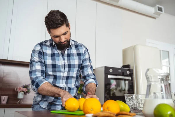 Attractive young man cutting orange in kitchen — Stock Photo, Image