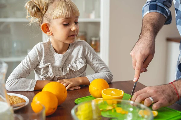 Adorable little girl watching how her dad cutting orange — Stock Photo, Image