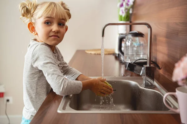 Niedliches kleines Mädchen wäscht Apfel unter laufendem Küchenhahn — Stockfoto
