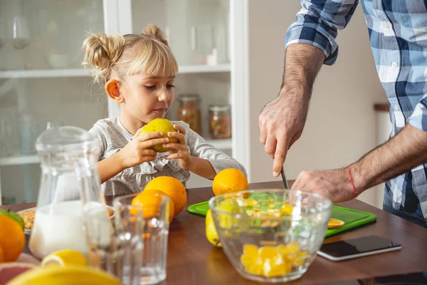 Niedliches kleines Mädchen, das Birne hält und beobachtet, wie Papa Orange schneidet — Stockfoto