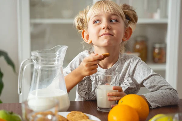 Adorable little girl holding cookie and glass of milk — Stock Photo, Image