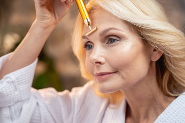 Relaxed mature woman applying a massager wand