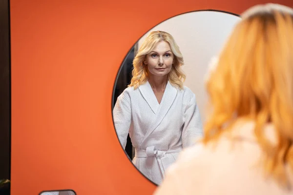 Serious Caucasian woman standing before a mirror — Stockfoto