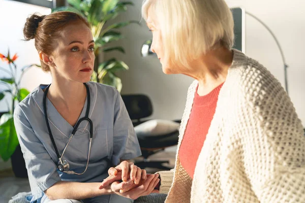 Geconcentreerde jonge arts ondersteunt haar volwassen patiënt — Stockfoto