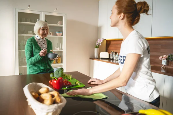 Delighted young volunteer cleaning kitchen for pensioner — Stock Photo, Image