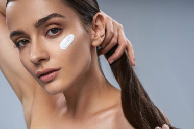 Çekici, hassas bir kız. Gri arka planda yüz bakımı yapıyor.